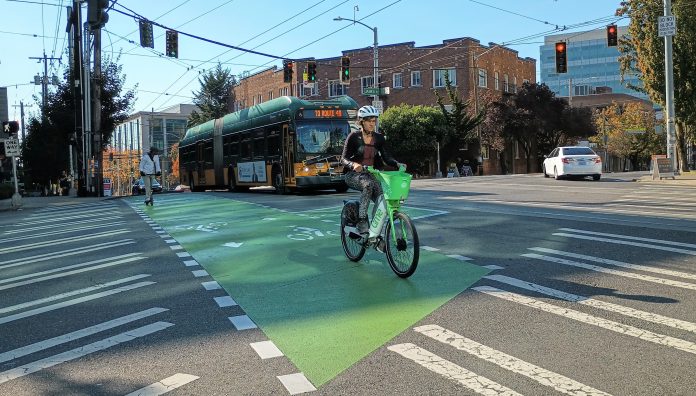 Broadway Someone riding a lime bike across a bike lane in Capitol Hill with a bus behind them