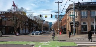 Someone on a bike crosses the street as pedestrians walk in a crosswalk and drivers wait to turn at Broadway and Pike in Seattle