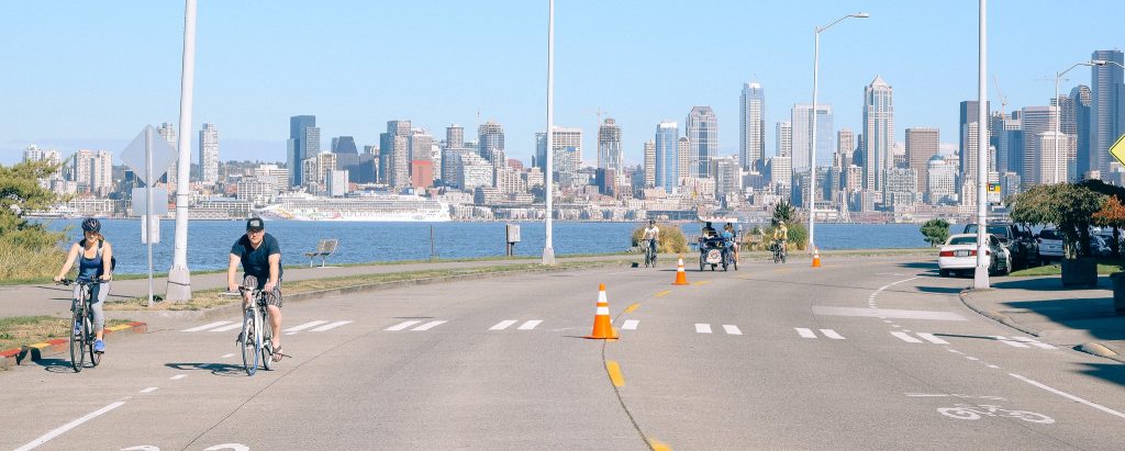 Two lane Harbor Avenue with the skyline of Seattle beyond the bay, people walking and rolling in the street