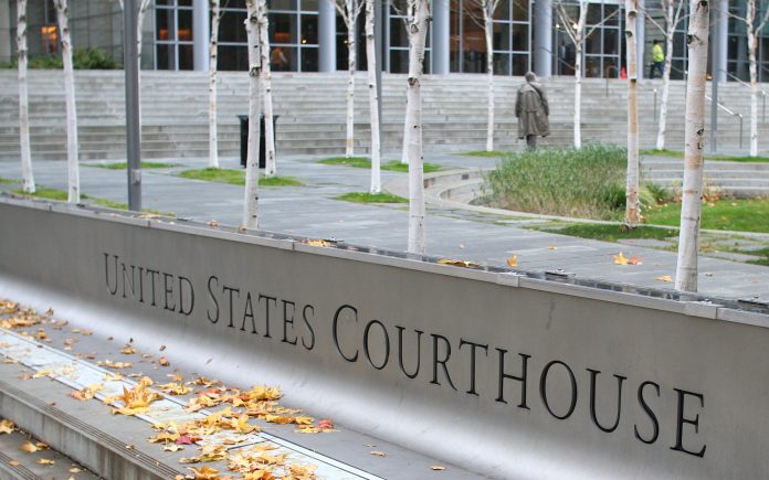 Sign for United States Courthouse, stairs and person walking to the entrance through skinny trees