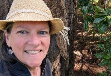 The Urbanist Welcomes a New Editor Linda Hanlon next to a tree and rhododendron bush.