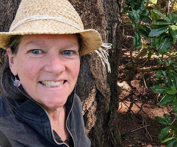 Linda Hanlon next to a tree and rhododendron bush.