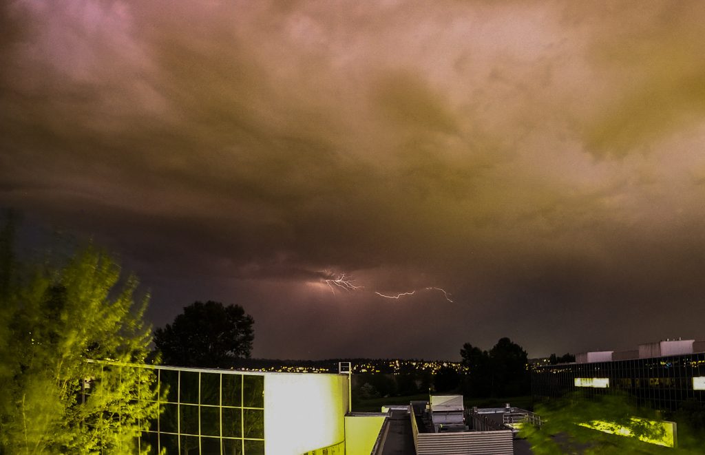 Dark sky and lightning over a modern high-rise building is related to an unseasonable May heatwave.