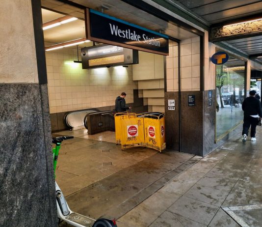 Sound Transit Restores Downtown Light Rail Service People walk by the station entrance, which includes a yellow barricade for a closed elevator.
