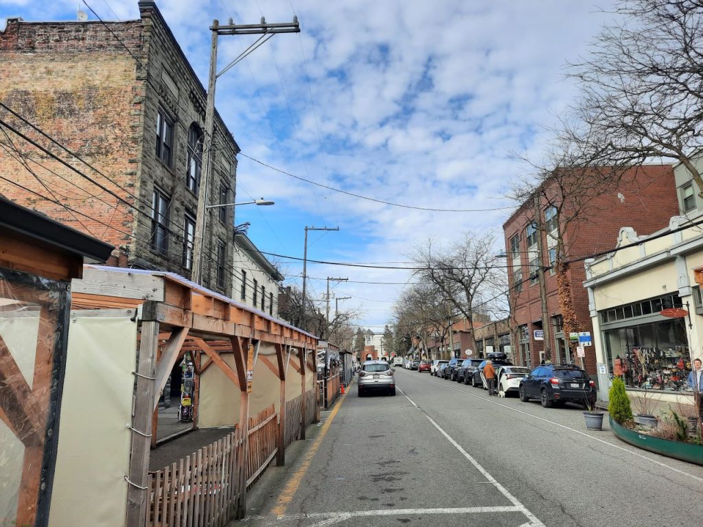 A view of Ballard Avenue looking north with pergolas on the left. A canoe planter decorates the one on the right.