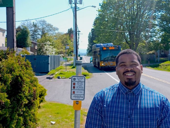 Joe Vinson stands on Military Road next to a crosswalk signal with a Route 156 bus in the background.