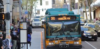 Route 301 using the 6th Avenue bus lanes in Downtown Seattle with a dozen riders waiting at a busy combined bus stop.