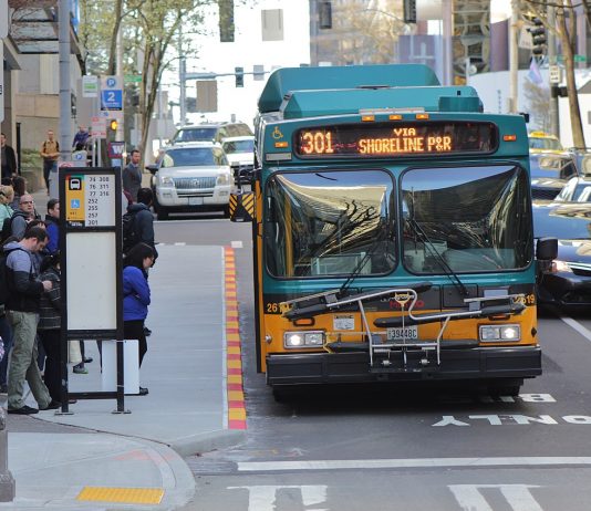 Metro Temporarily Suspending Six More Bus Routes This Month Ahead of September Cuts Route 301 using the 6th Avenue bus lanes in Downtown Seattle with a dozen riders waiting at a busy combined bus stop.