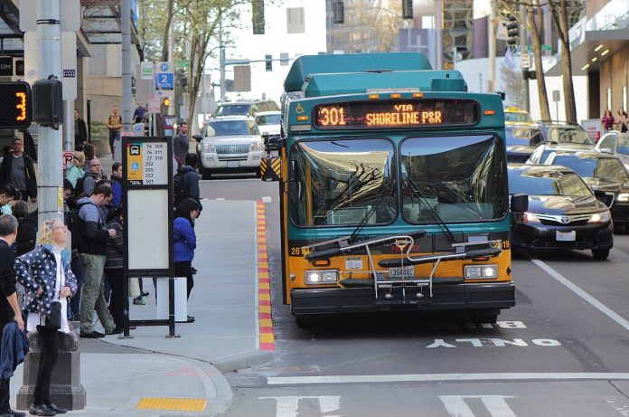Route 301 using the 6th Avenue bus lanes in Downtown Seattle with a dozen riders waiting at a busy combined bus stop.