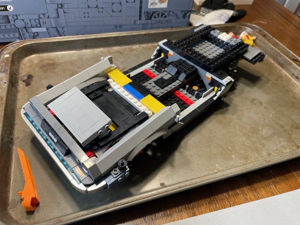 Partially built lego car on a sheet pan. Front quarter panels in silver are complete, rest is open.
