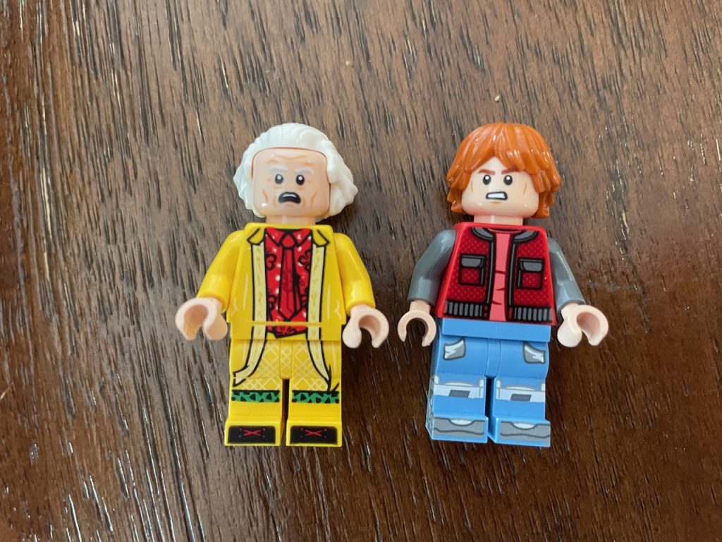 Two Lego minifigs from Back to the Future, left is in yellow with white hair and gasping. Right is in a vest with bright red hair and a scowl looking vaguely Eric Stoltz-like.
