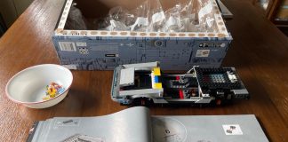 Partially built lego car with open instructions and a box full of bags of legos.