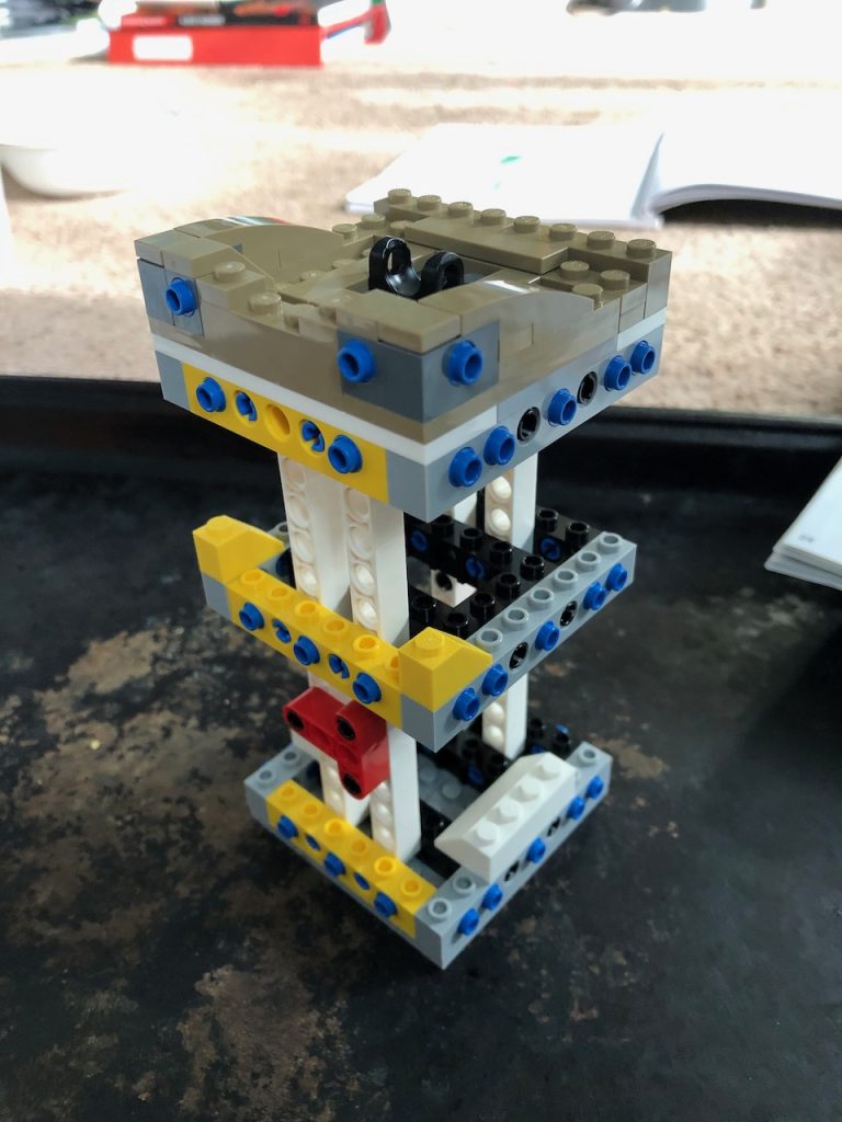 Three level square tower of white and yellow legos.