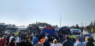 King County Executive Dow Constantine speaks at a podium in front of a row of busses flanked by Metro employees.