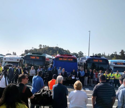 Metro Gears Up To Tackle Its Worker Shortage King County Executive Dow Constantine speaks at a podium in front of a row of busses flanked by Metro employees.