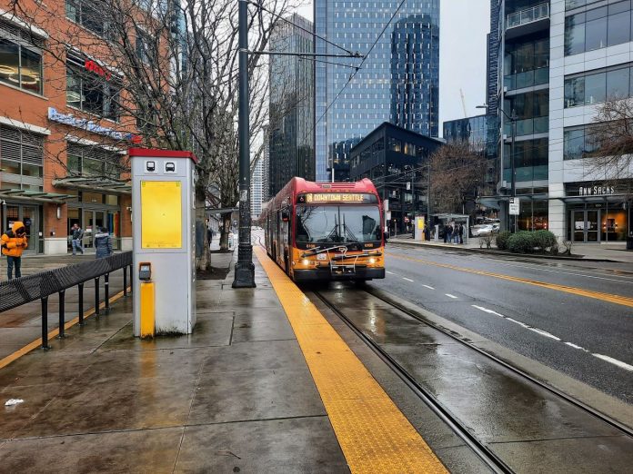 A RapidRIde C bus pulls up to the transit stop in front of Whole Foods at Denny Way intersection on a wet afternoon.