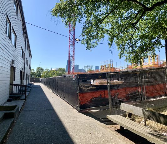 Black History and Ambition Meet at an Expanding Bryant Manor Existing housing separated by a sidewalk from a large construction site with crane.