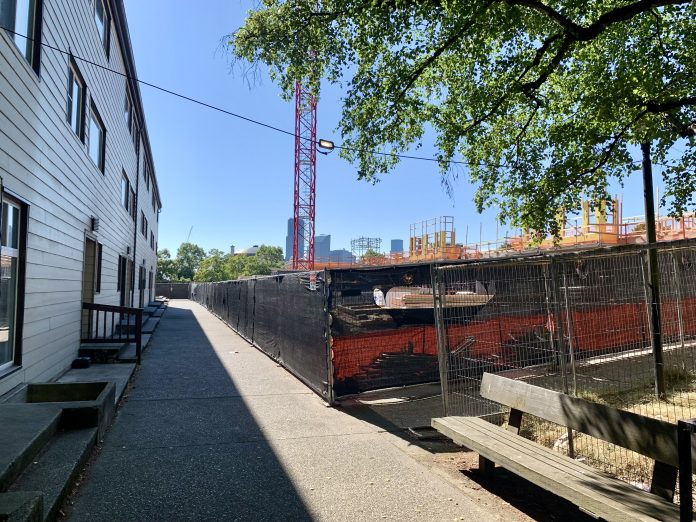 Existing housing separated by a sidewalk from a large construction site with crane.