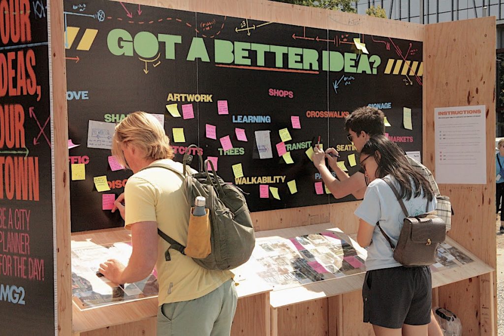 Young adults writing post-it notes about city planning and displaying them on a board titled, Got a Better Idea?