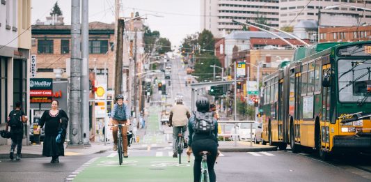 People ride bikes along Broadway. The bustling business district in Capitol Hill blends bike lanes, pedestrian spaces, bus service, streetcar tracks, and vehicle traffic.