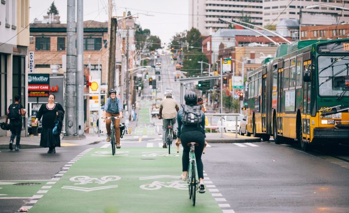 People ride bikes along Broadway. The bustling business district in Capitol Hill blends bike lanes, pedestrian spaces, bus service, streetcar tracks, and vehicle traffic.