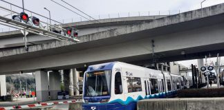 A light rail train in SoDo passes under highway overpasses and enters an intersection.