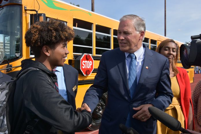 Governor Inslee shakes the hand of a Tacoma high school student standing in front of the state's first electric school bus in 2019.