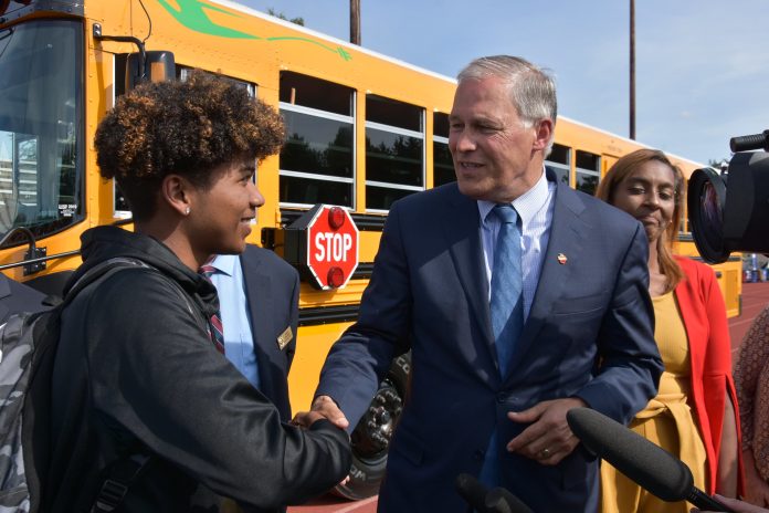 2019 Inslee Bus Grants_Credit Govs Office Governor Inslee shakes the hand of a Tacoma high school student standing in front of the state's first electric school bus in 2019.