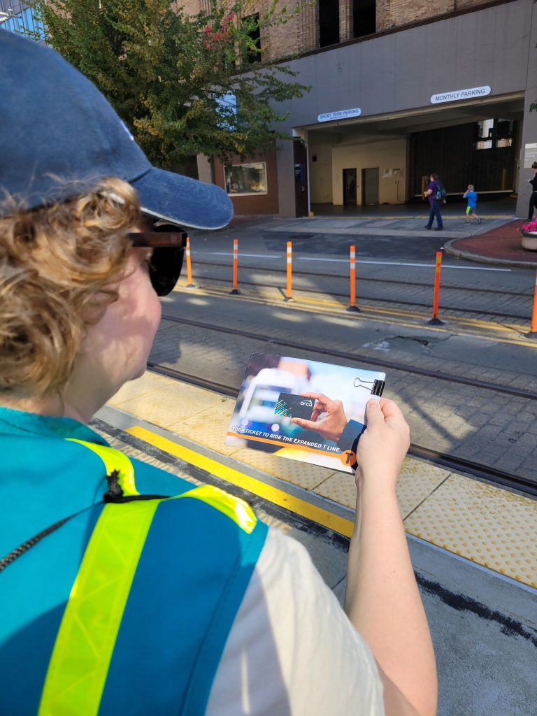 Looking over the shoulder of a Sound Transit staff person at her hand holding free orca cards and how to use them at one of the new T-Line stations.