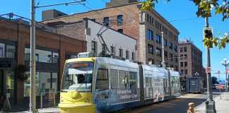 Yellow front of a streetcar passing in front of brick buildings.
