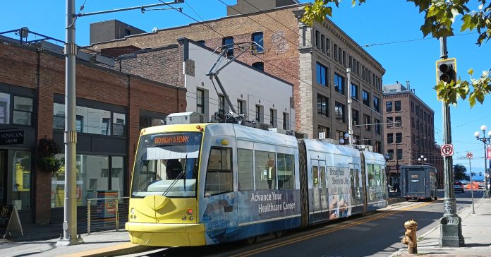 IMG_20230914_120846076 Yellow front of a streetcar passing in front of brick buildings.