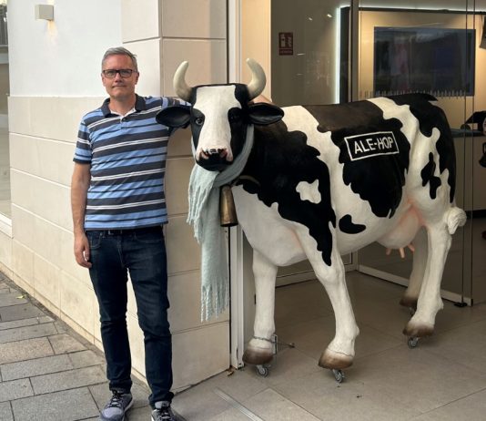 Meet Ray Delahanty, the Guy Behind CityNerd Ray poses with a life-size cow sculpture while traveling in Spain. Ray wears glasses and has sandy-colored hair.