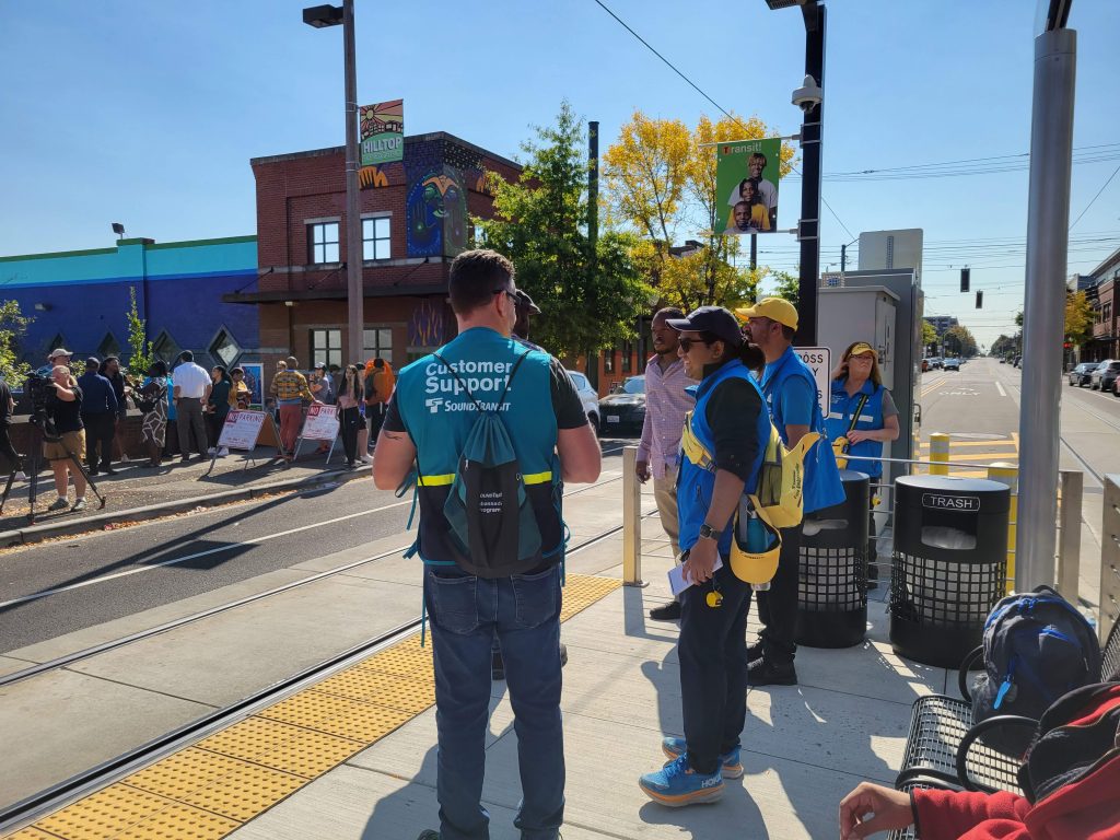 Sound Transit staff in colorful blue and green shirts wait for a streetcar at the Hilltop Station.