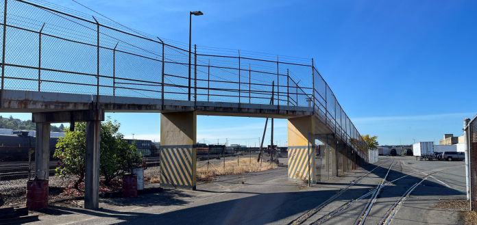 Fenced ramp to a multi-use path bridge over the Interbay railroad tracks.