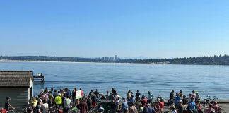 The Results Are In on The Urbanist’s First Annual Reader Survey A group of about 50 bicyclists stand on the shores of Lake Washington with Bellevue in the background.