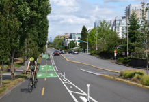 Bellevue Seeks Public Feedback on 15 Miles of New Bike Infrastructure Looking down NE 12th Street with a rendering of a cycletrack with painted lines, green painted boxes and flexible posts.