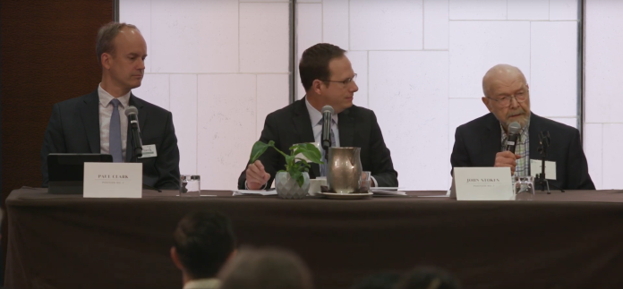 Men in suits at a table with a white background.