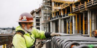 A construction works cuts rebar with the elevated station structure in the background.