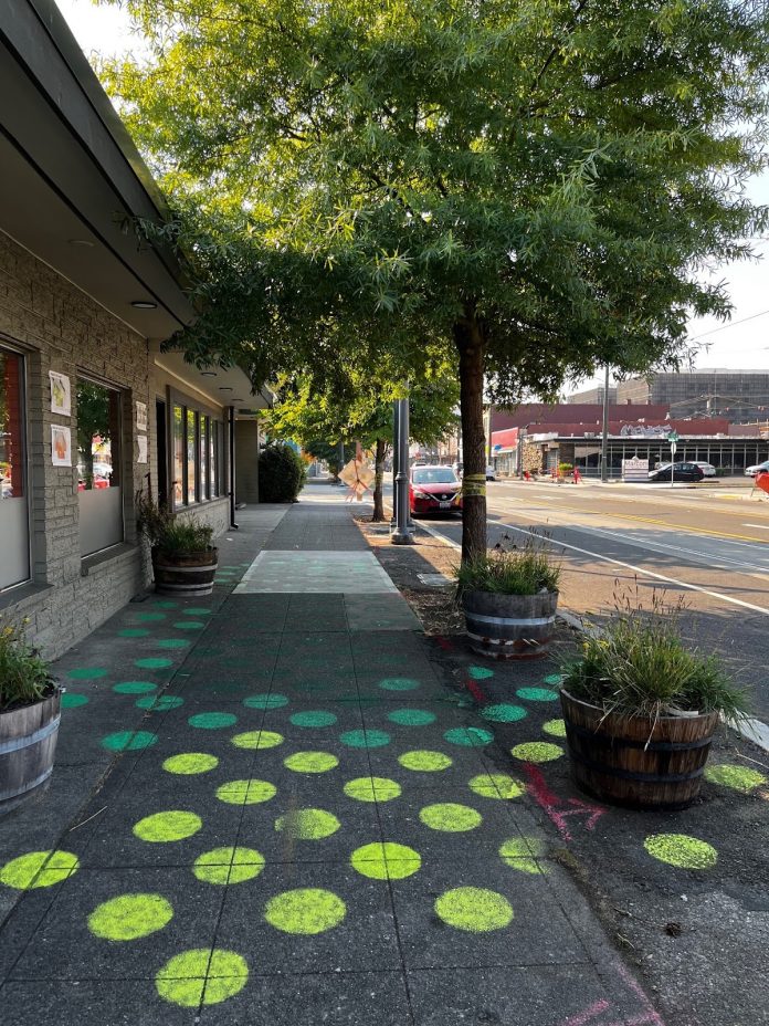 Green street trees shade Tacoma sidewalks. Colored dots on the sidewalk represent the values of the cooling effect.