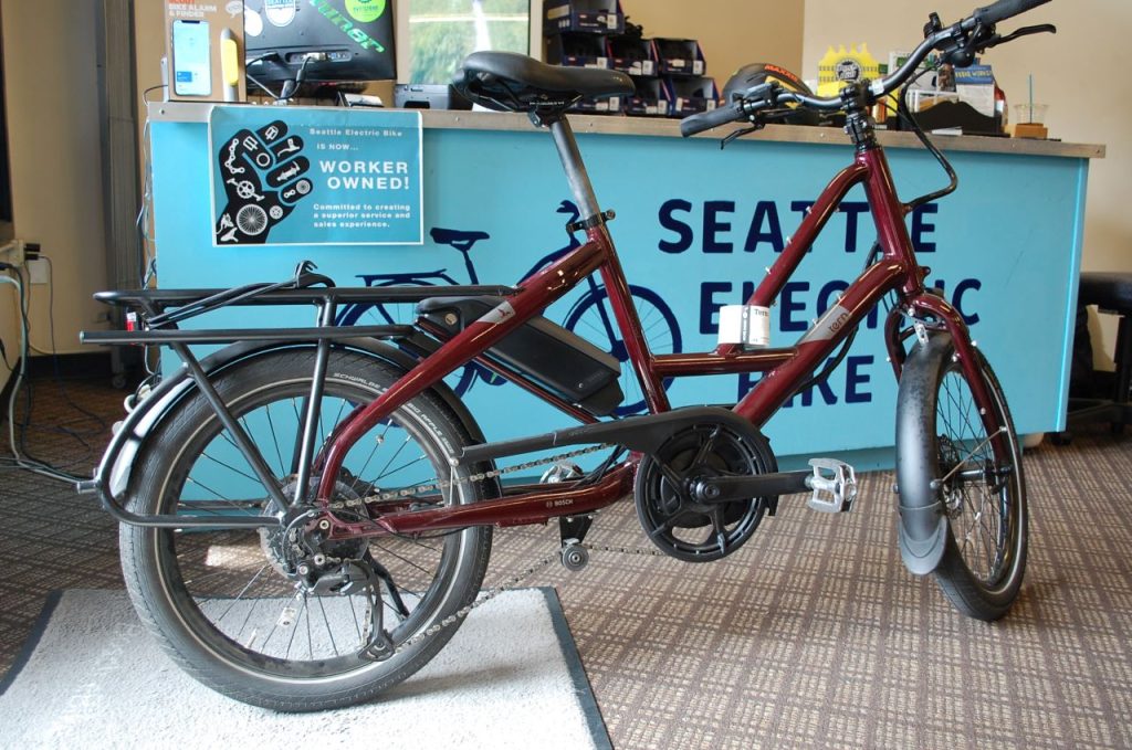 A maroon cargo bike is in from the turquoise-colored sales counter at the bikeshop.