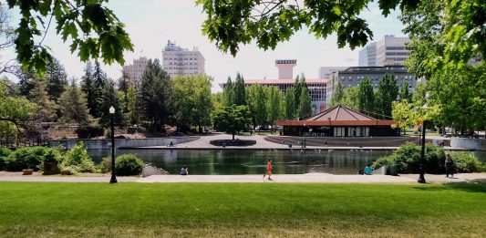 People stroll and jog in Waterfront Park with the Spokane skyline in the background.