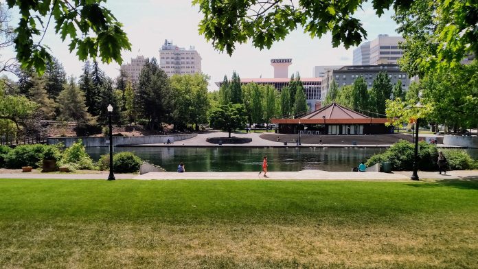 People stroll and jog in Waterfront Park with the Spokane skyline in the background.