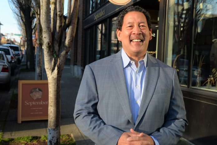 Mayor Harrell smiles in a gray suit outside a brick storefront.