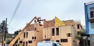 Franz: Mobilize Washington State-Owned Land to Tackle Housing Affordability Crisis A small crane move materials to the top of a three story townhome complex where a construction work receives them.