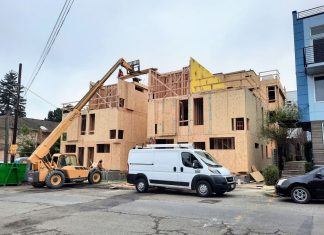 Seattle’s Housing Construction Booms While Permitting Flashes Warning Signs A small crane move materials to the top of a three story townhome complex where a construction work receives them.