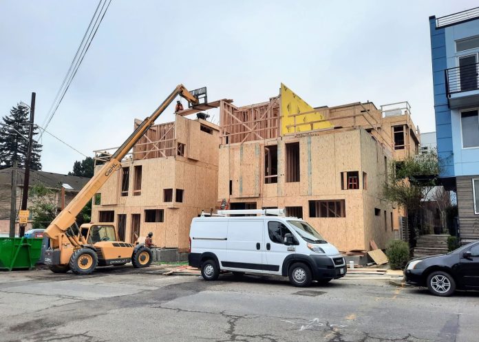 A small crane move materials to the top of a three story townhome complex where a construction work receives them.