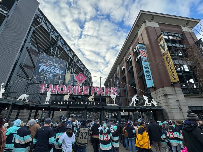 Entrance gate to T-Mobile Park with crowd going through ticketing, looking upward towards soft clouds and banners for Vegas and Seattle.