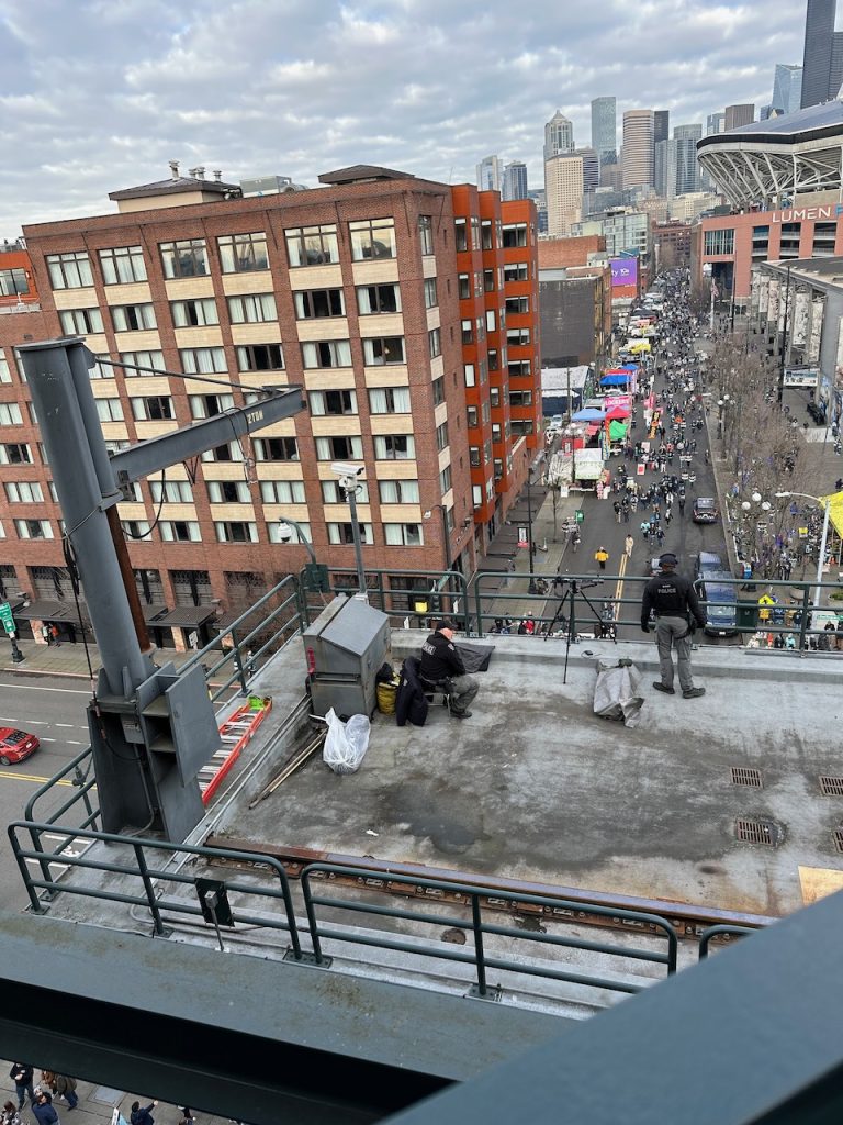 View looking down on people moving down a crowded street lined with food trucks, with police watching in the foreground.