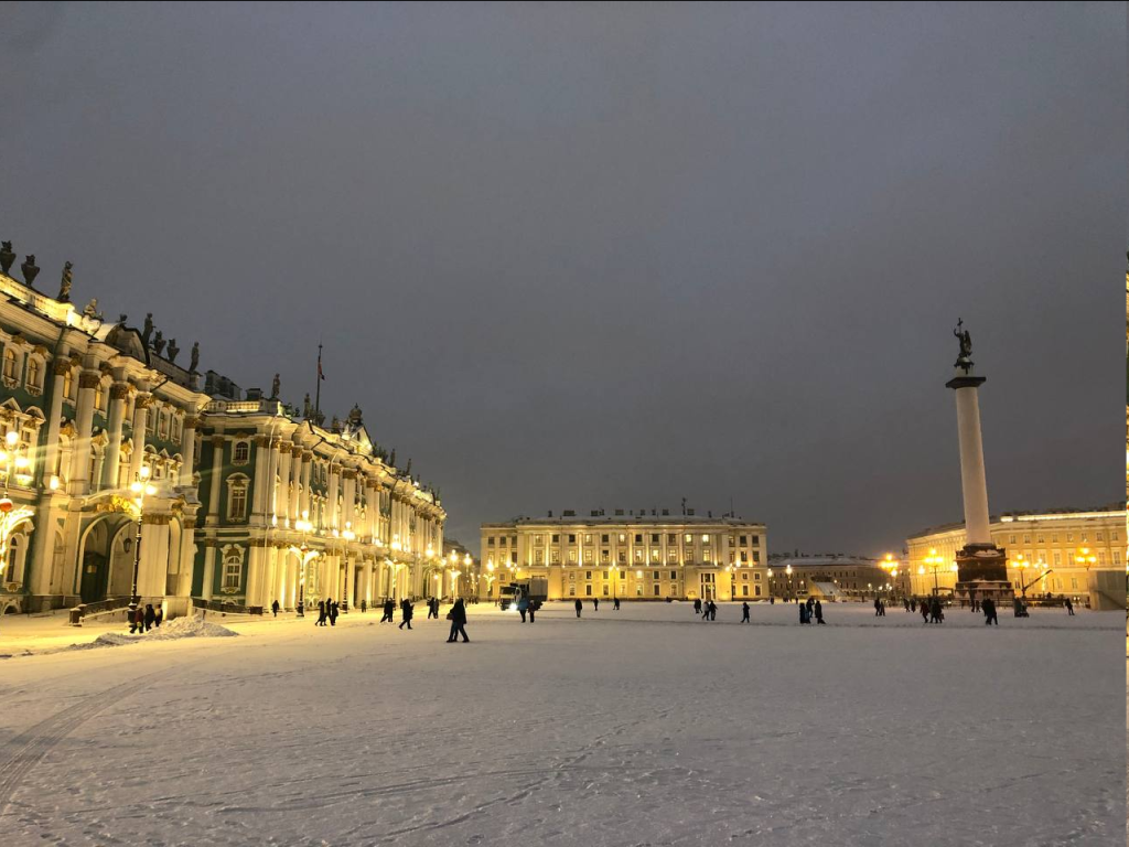 Pedestrians walk a large square with an statue tipped obelisk in the center and the long wings of the museums flanking the square.