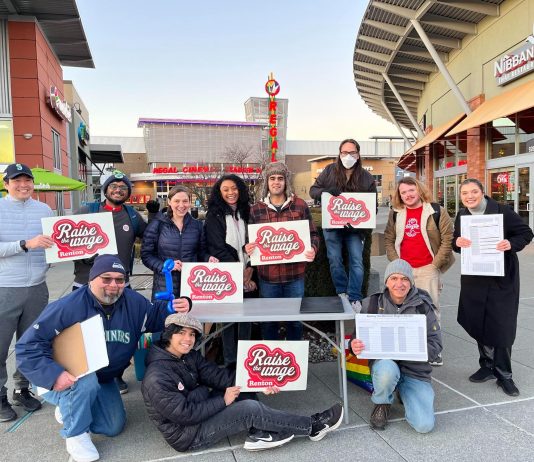 Voters Set to Decide on Raise The Wage Renton in February Ballot Measure A group of about 15 campaign volunteers hold clip board and campaign signs at a mall plaza.